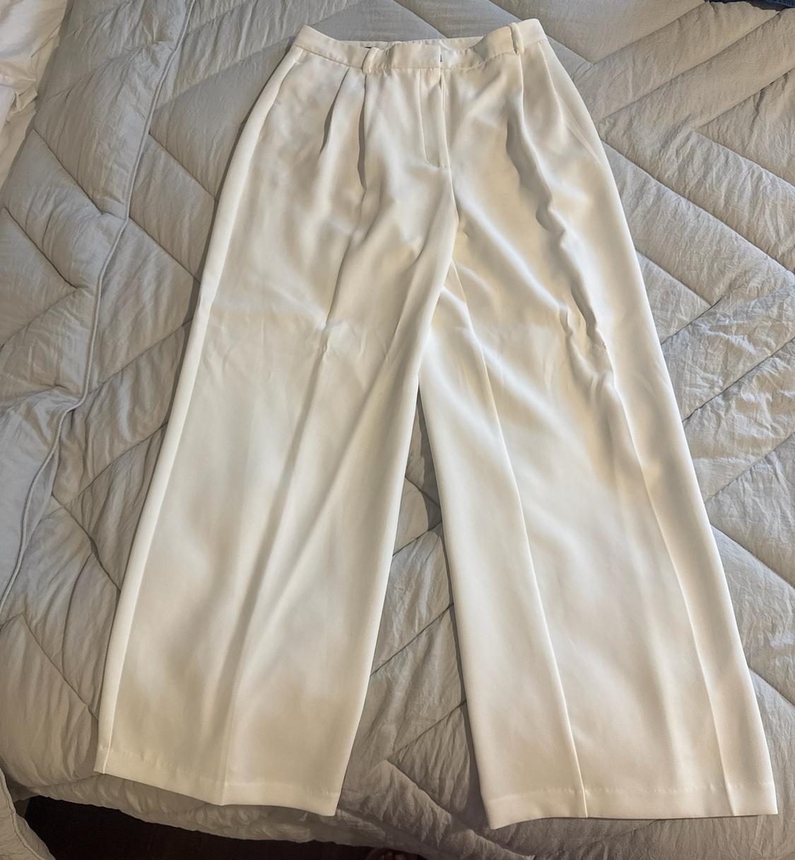 White wide-leg, pleated trousers, laid out on a bed with a light grey quilted duvet.