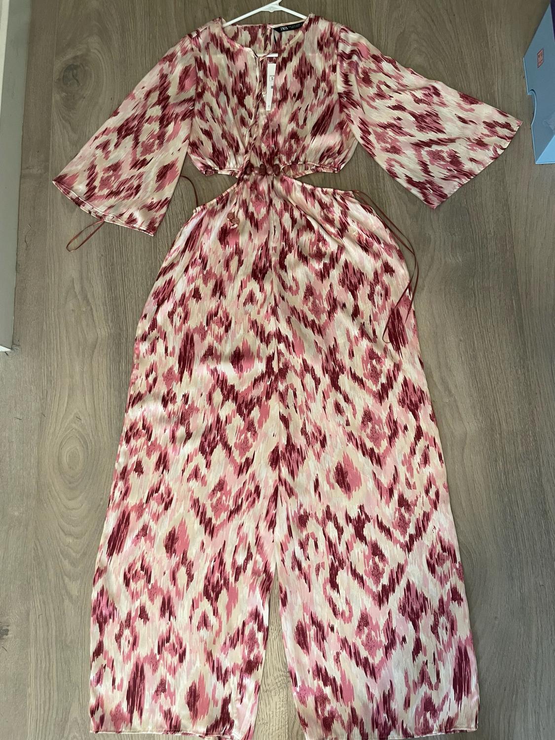 Long jumpsuit with a print in shades of pink and burgundy with cut-outs at the waist and wide sleeves, on a wooden floor.