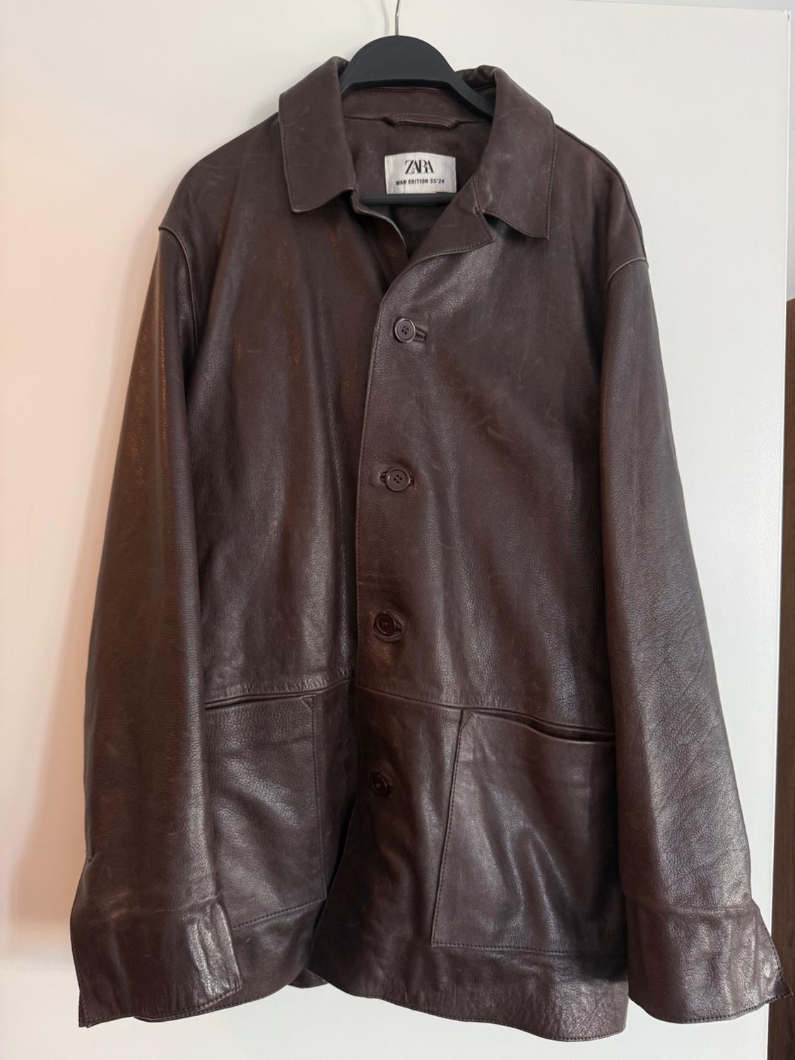 Brown leather jacket hanging on a black hanger. Visible tag with text: "ZARA MAN EDITION 1974".