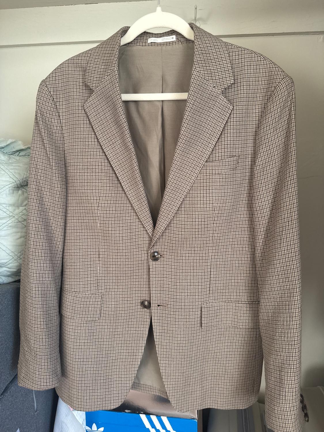 Brown and white plaid jacket hanging on a white hanger, with two buttons and front pockets. Wardrobe staple.