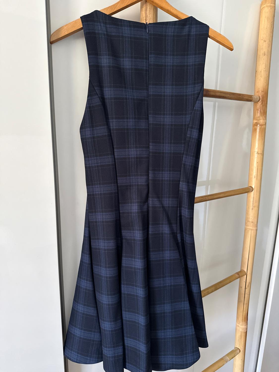 Sleeveless blue and black check dress hanging on a wooden hanger on a bamboo ladder.