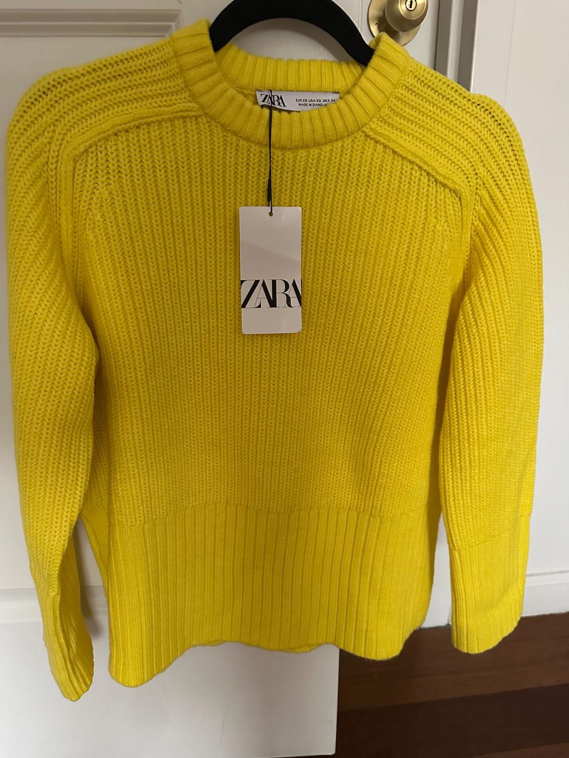 Yellow chunky knit sweater hanging on a black hanger. White tag with the text "ZARA" visible in the center.