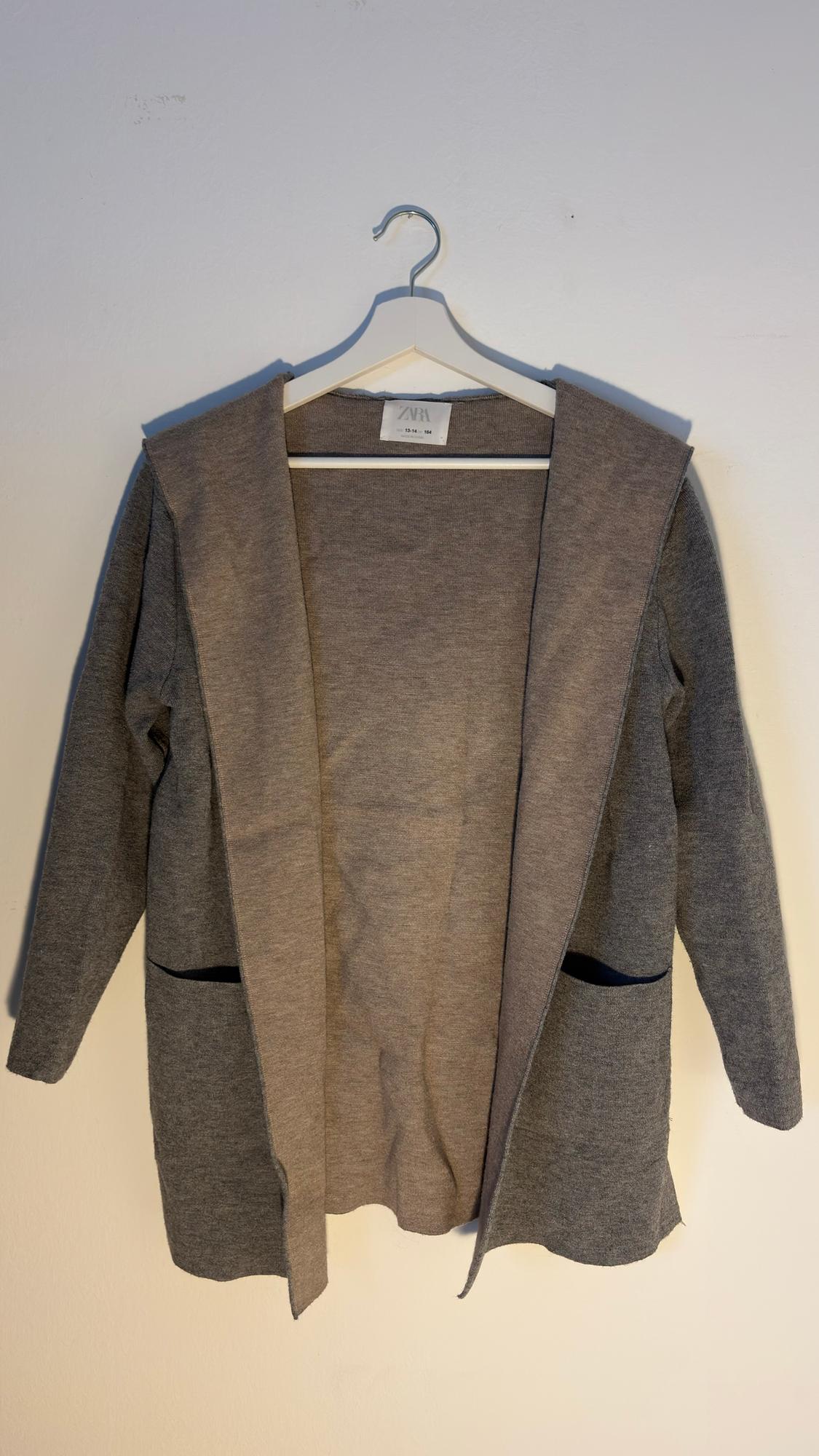 Grey knitted jacket hanging on a white hanger, with a visible "ZARA" label. Plain white background.