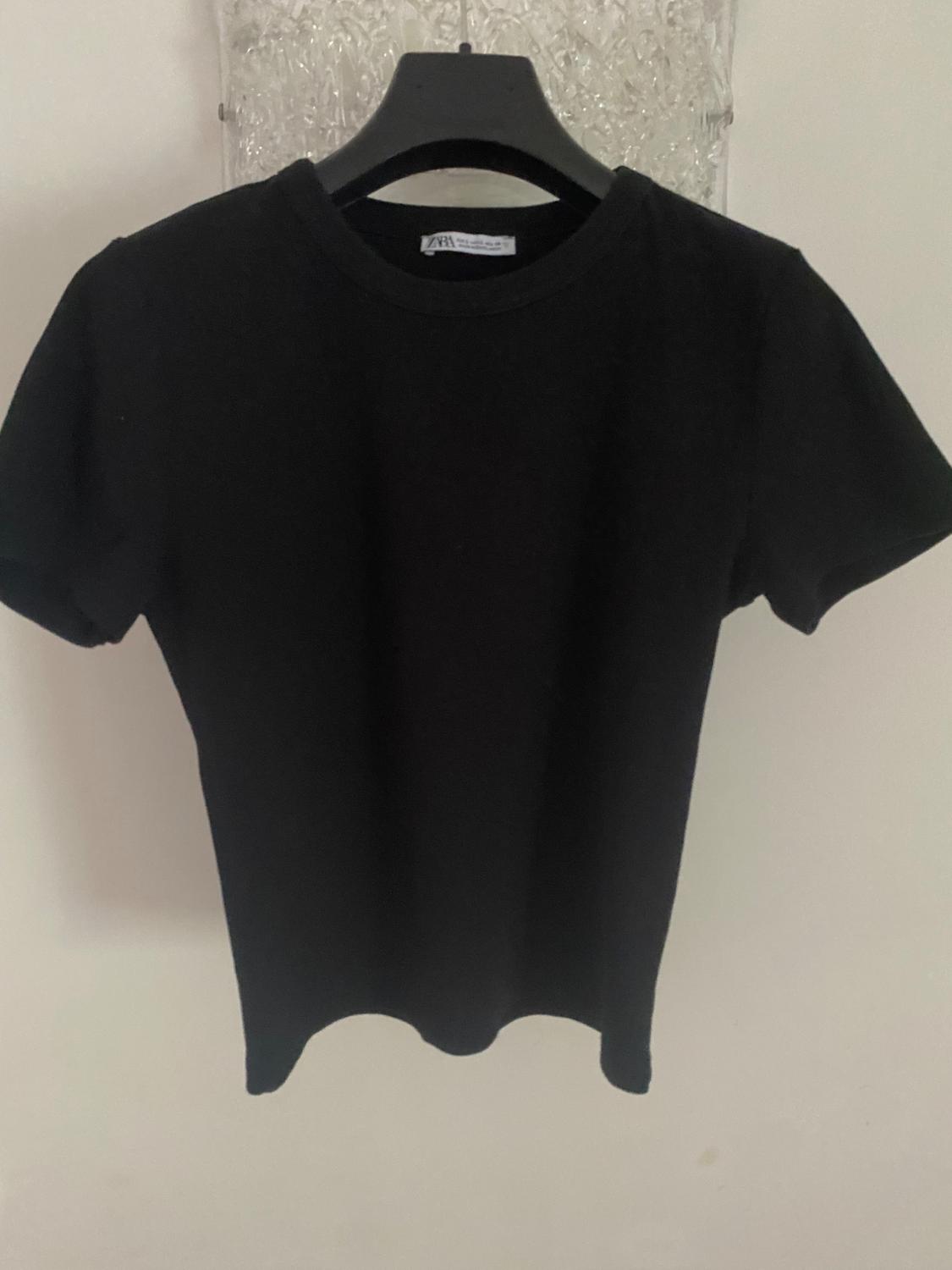 Black short-sleeved t-shirt hanging on a black hanger, against a textured white background.