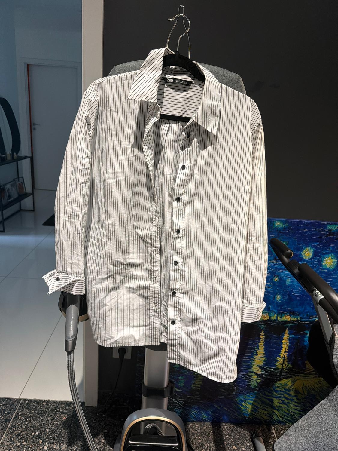 Black and white striped shirt hanging on a hanger over a chair, with a dark wall background and a colourful picture.