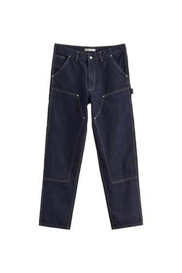 Dark blue denim trousers with contrasting stitching and reinforced panels on a white background. Inner label with ZARA text.