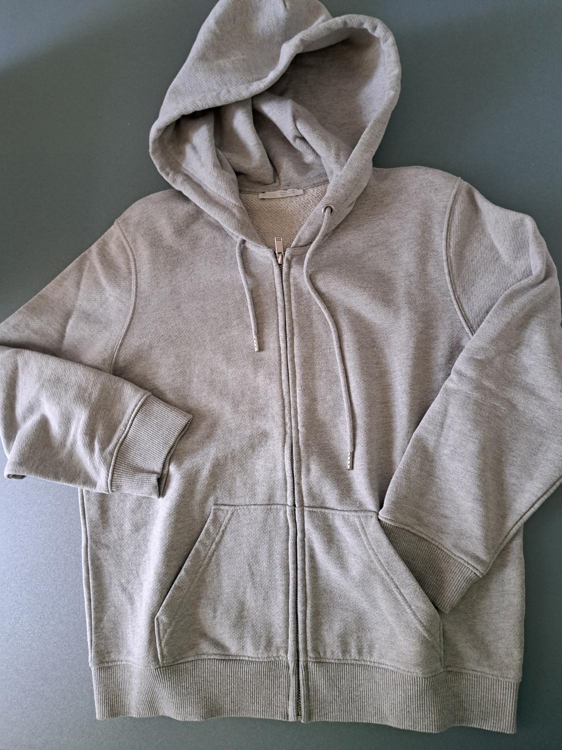 Grey hooded zip-up sweatshirt on a grey background. Visible front pockets and adjustable drawstrings.