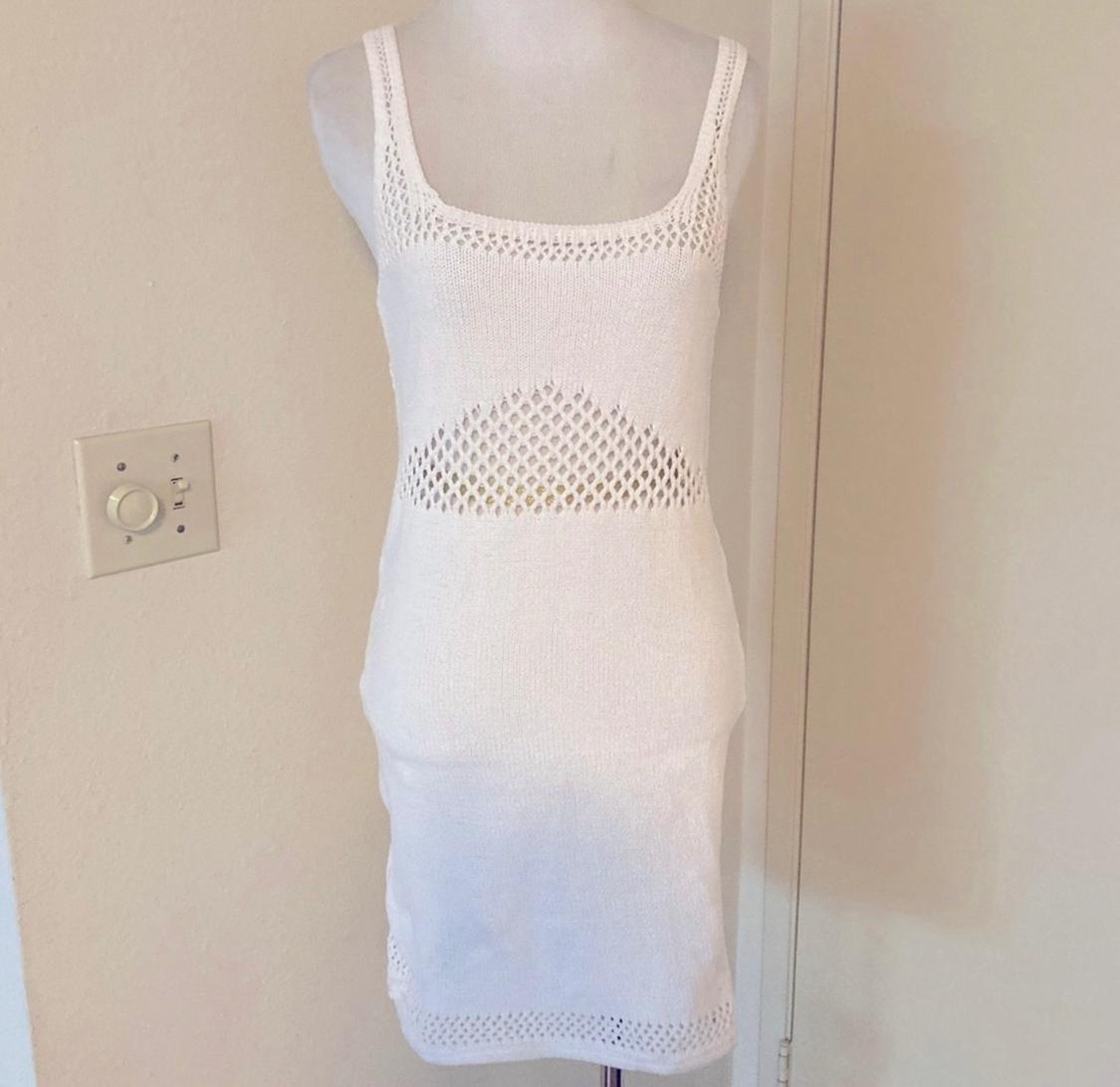 Mannequin in a white strappy dress, with an openwork knit on the chest and waist, against a beige wall background with a visible light switch on the left.