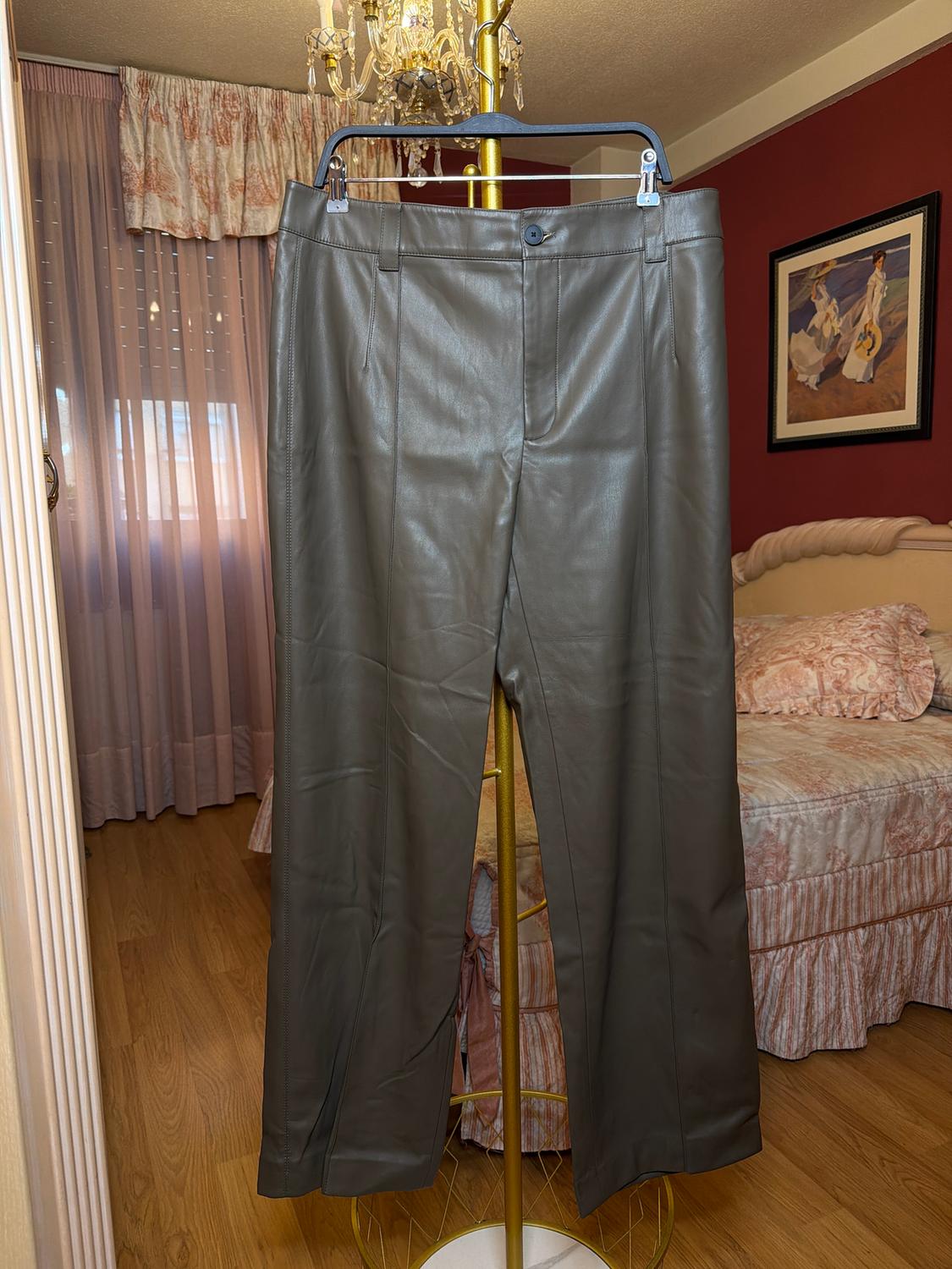 Brown leather trousers hanging on a gold clothes rail in a room with pink curtains and a chandelier.