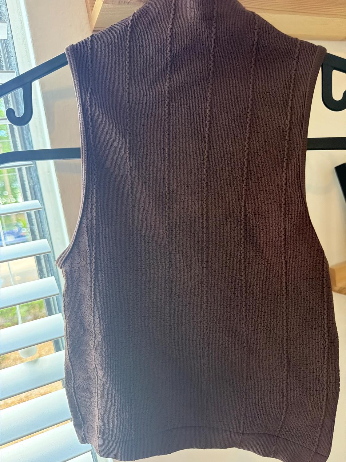Dark brown sleeveless mock neck top with vertical line texture, hanging on a black hanger in front of a window with blinds.