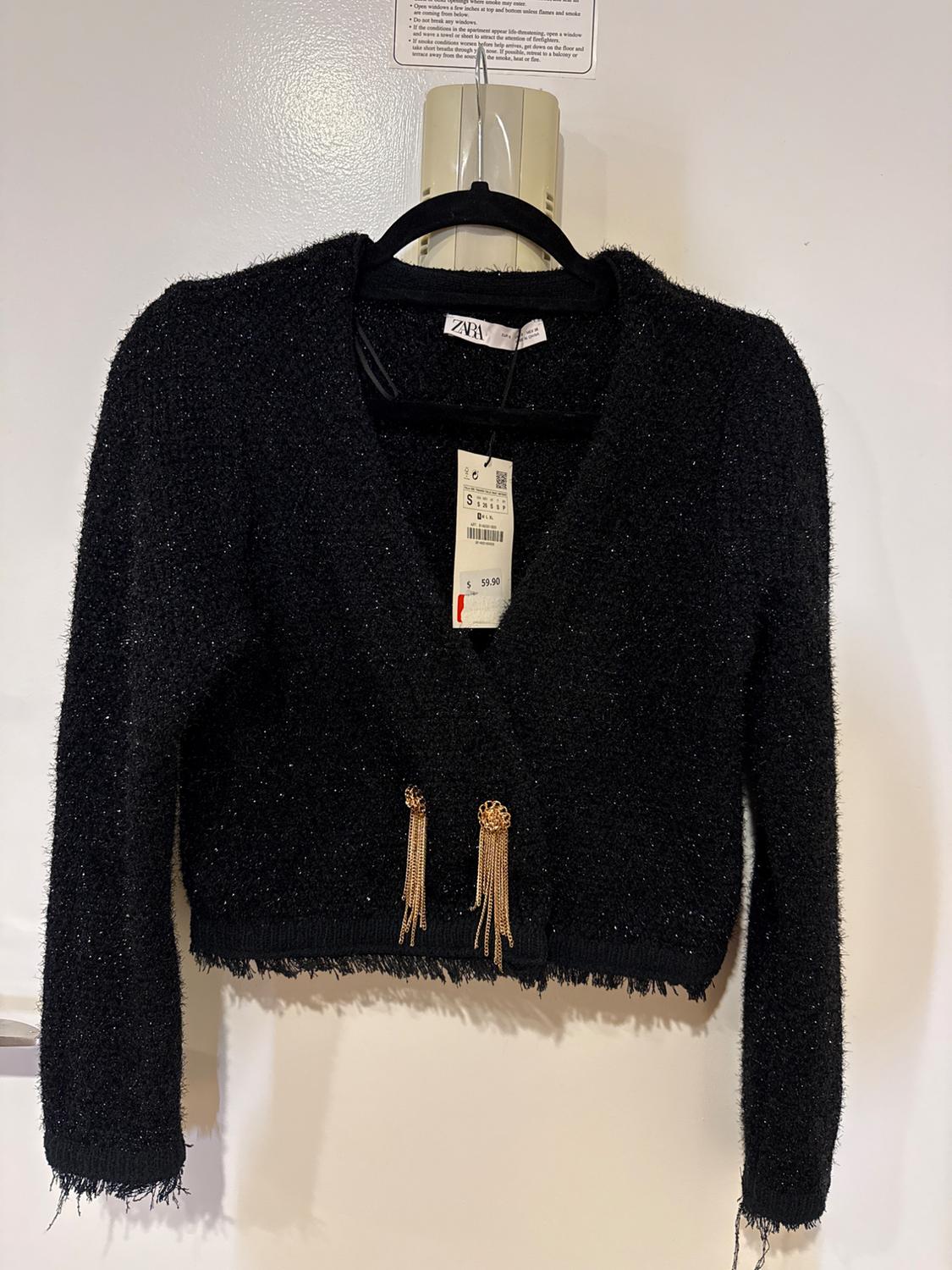 Black knitted jacket with dangling gold details, hanging on a hanger. Visible tag with price of $59.90.
