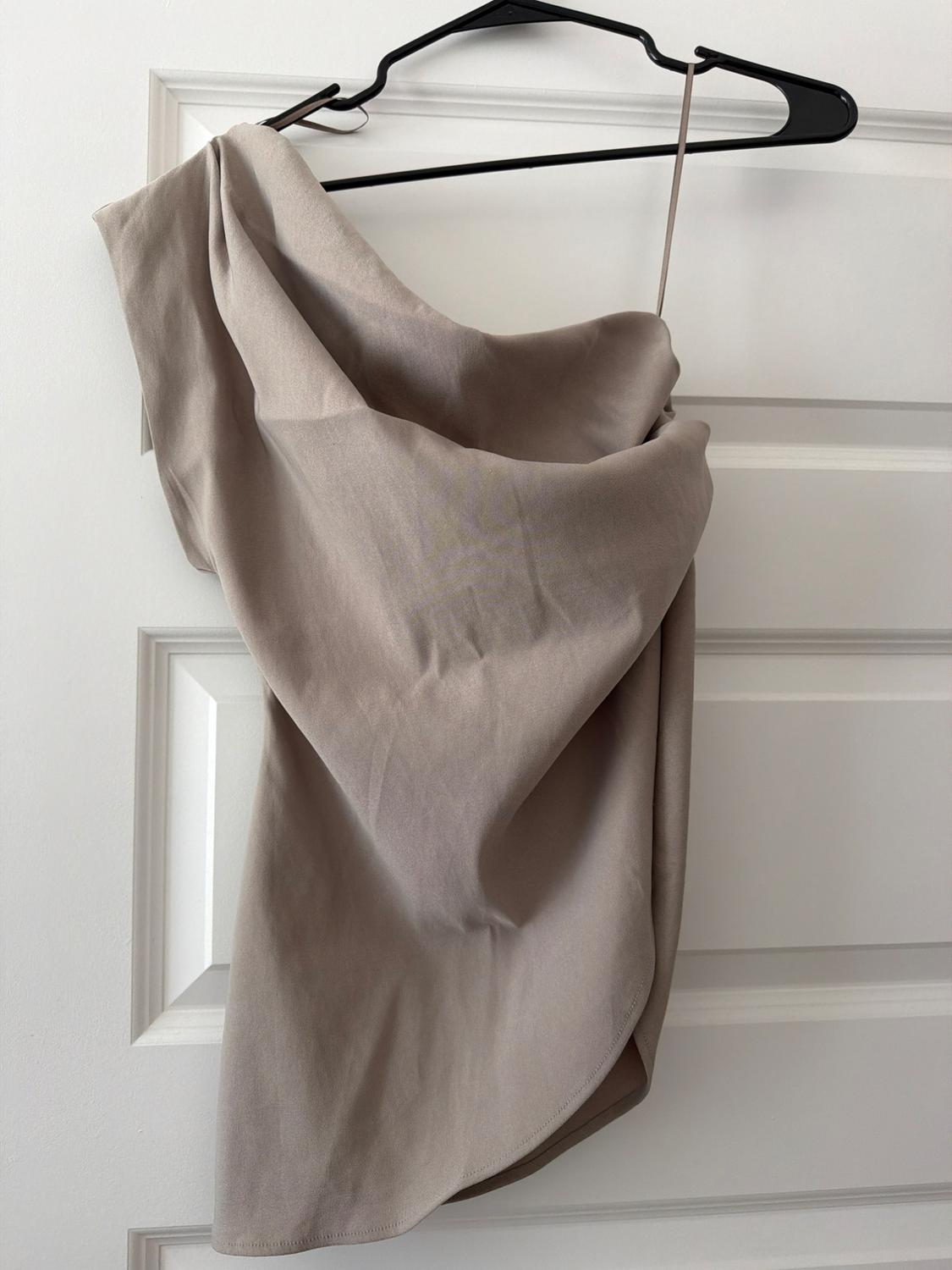 Beige asymmetric drape top, hanging on a black hanger on a white door.