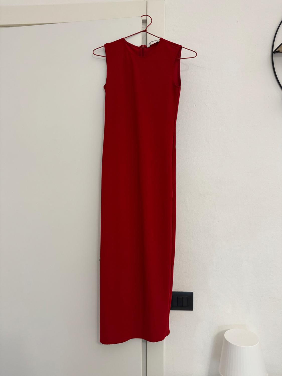 Sleeveless red dress hanging on a hanger over a white door. To the right, a white lamp on a table.