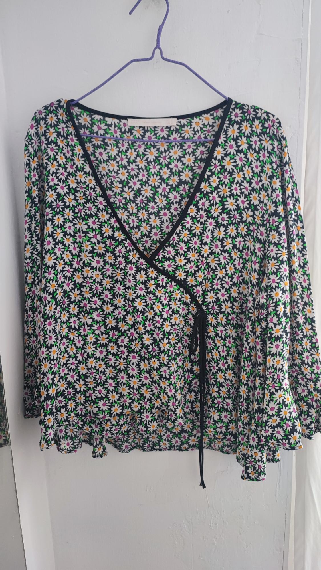 Long-sleeved blouse with small floral print in white, yellow, and pink on a black background, hanging on a hanger.