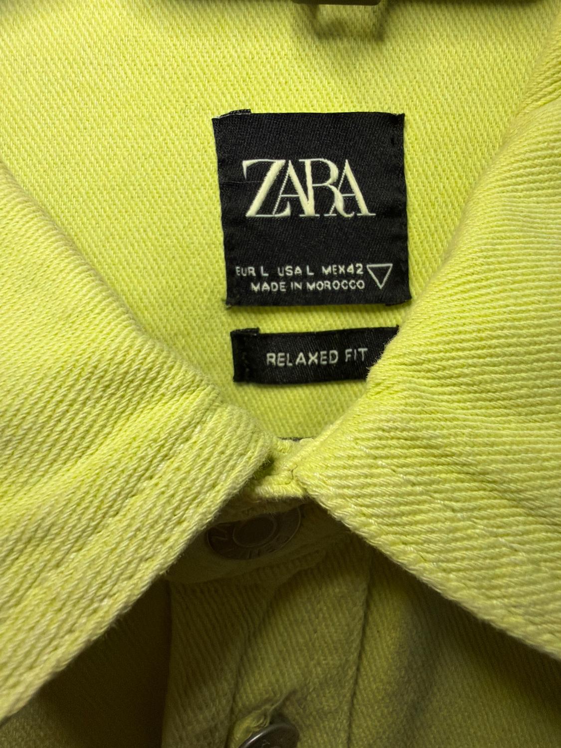 Yellow shirt label with text: "ZARA, EUR L USA L MEX 42, MADE IN MOROCCO, RELAXED FIT". Visible textured fabric.