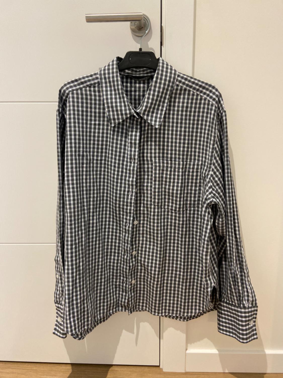 A black and white checked shirt hanging on a black hanger over a white door. The shirt has buttons and a pocket.