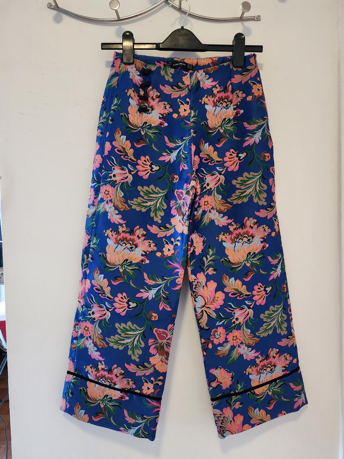 Front view of blue pants with a floral print in pink and green tones.