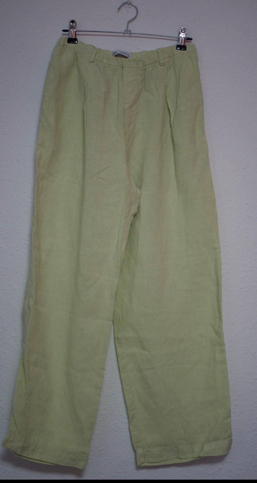 Wide-leg light green trousers with pleats and an elasticated waist, hanging on a metal hanger against a white wall.