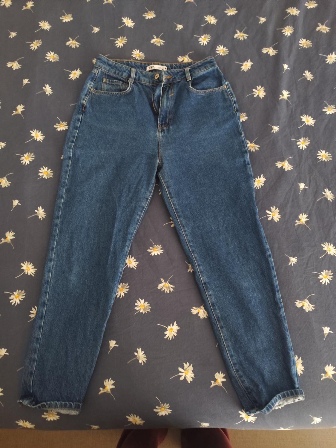 Blue jeans on a grey duvet with a white and yellow daisy print.