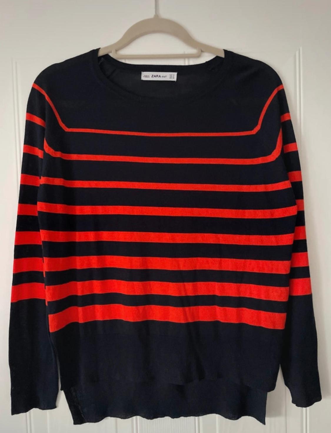 Dark long-sleeved jumper with red horizontal stripes hanging on a white coat hanger. The label reads ZARA KNIT.