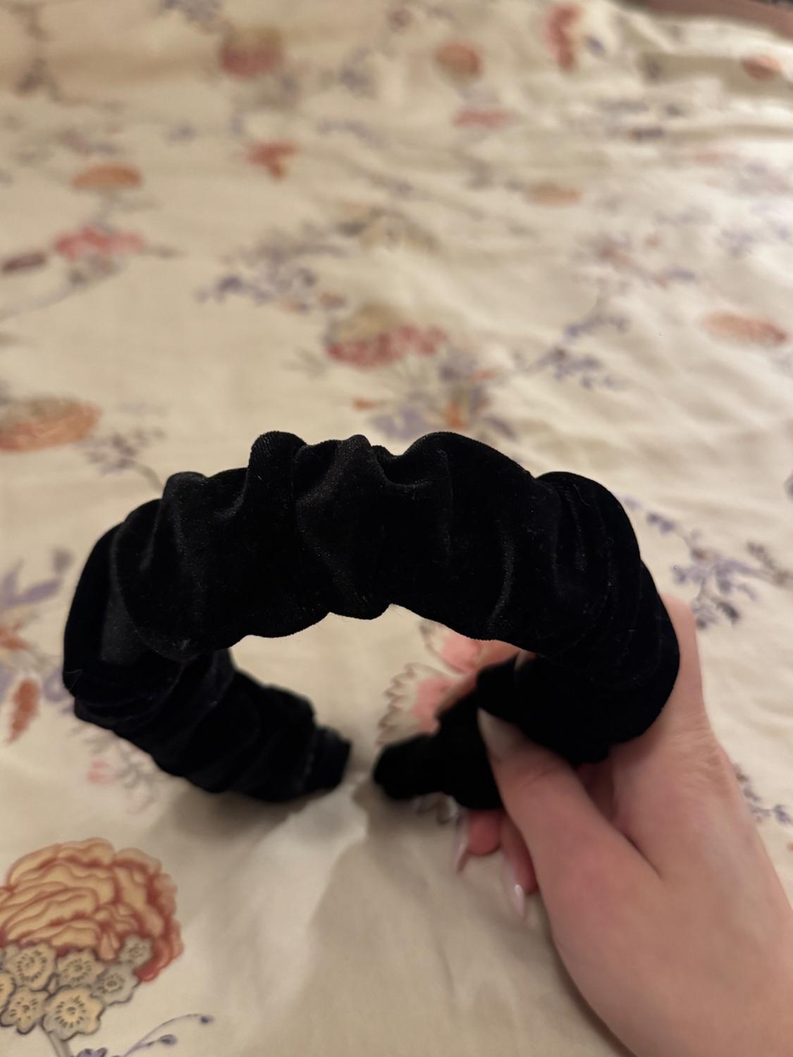 A black velvet headband held by a hand over a floral-patterned fabric in pastel tones.