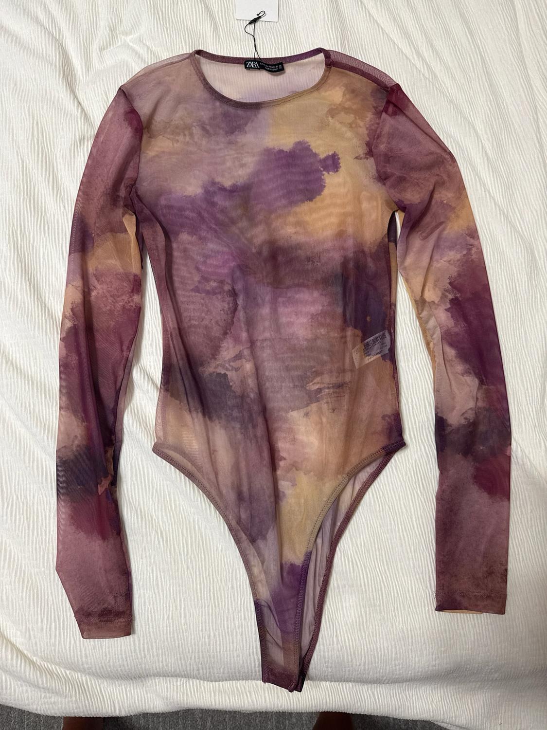 Semi-sheer long-sleeve bodysuit featuring an abstract purple and beige print on a textured white background. ZARA label on the collar.