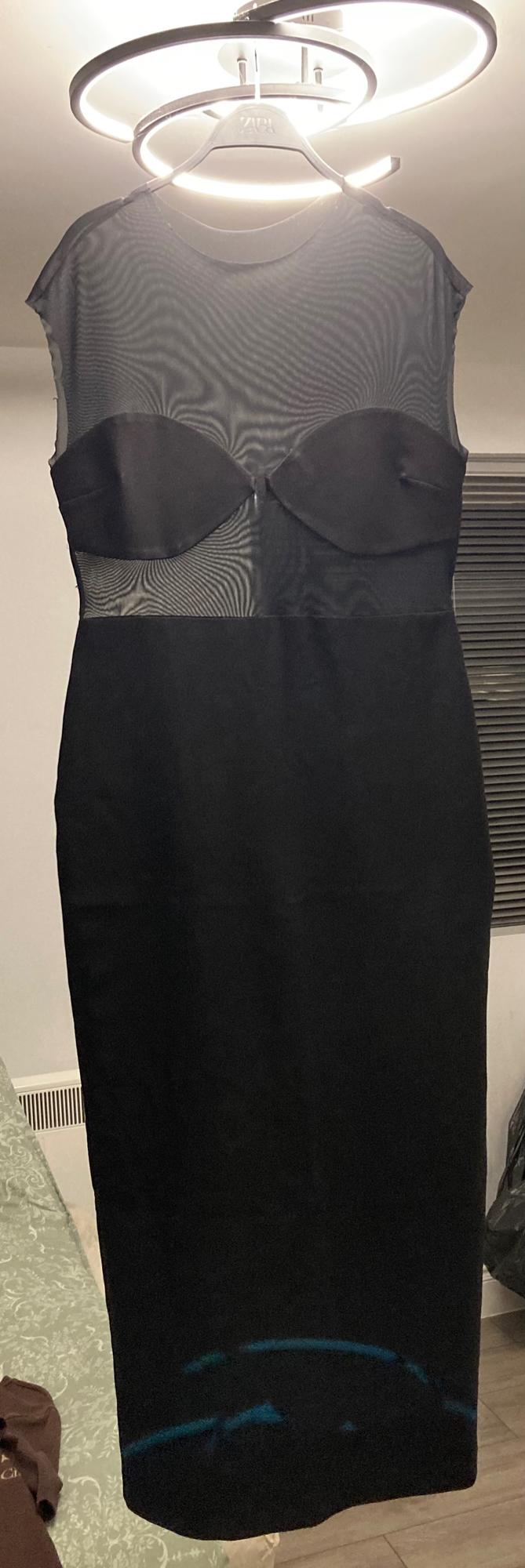Sleeveless black dress with a sheer top and structured cups, hanging on a hanger under bright circular light.