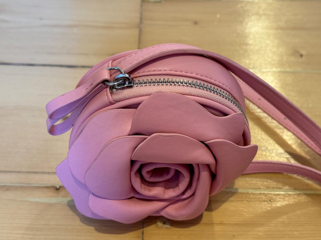 Pink flower-shaped handbag with a zip fastening and matching strap, on a light wooden surface.