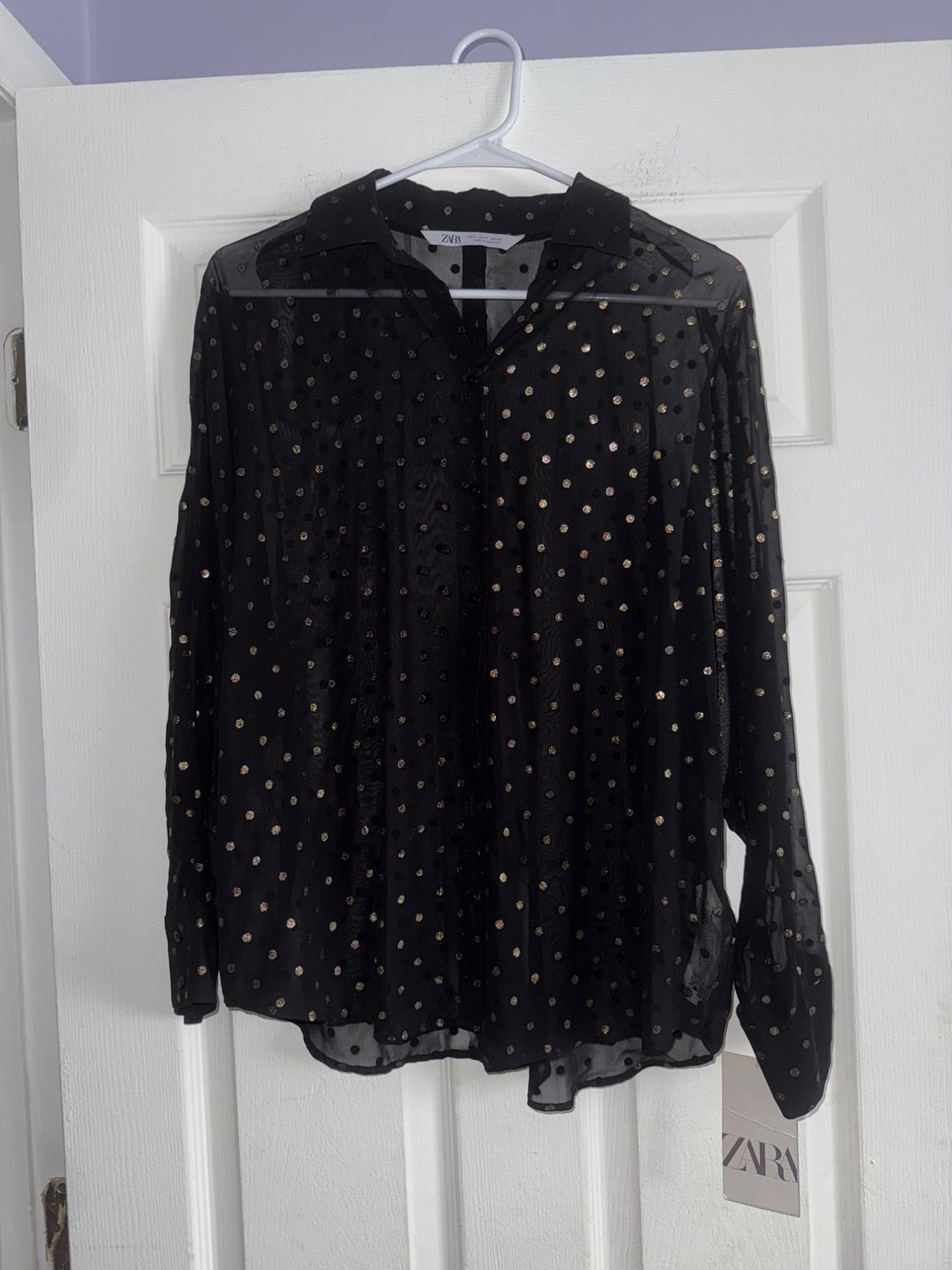 Sheer black shirt with gold polka dots hanging on a white door. Visible label with the text "ZARA".