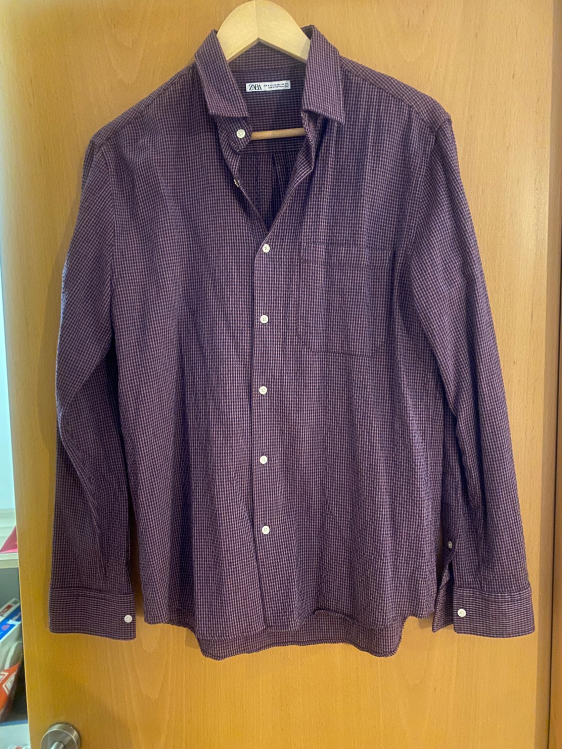 Small checked shirt in shades of brown and white, hanging on a wooden hanger over a light wood door.