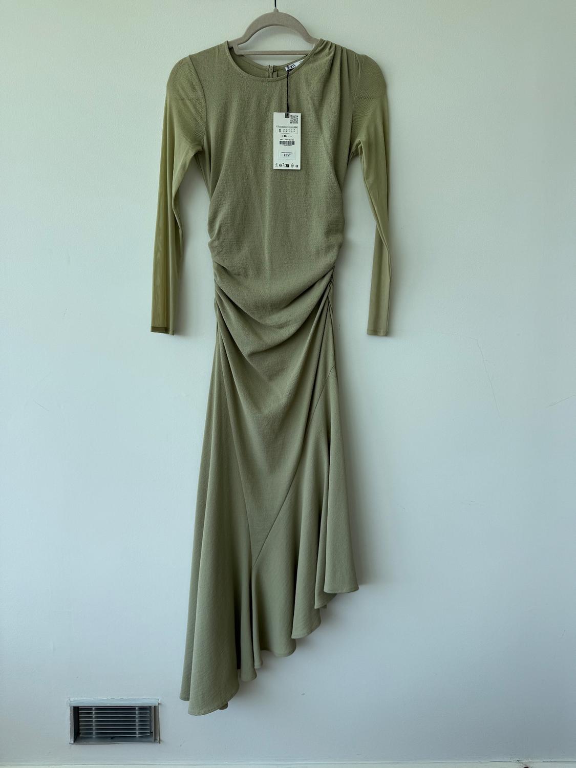 Olive green long-sleeved dress hanging on a hanger against a white background. Label visible in the centre of the dress.