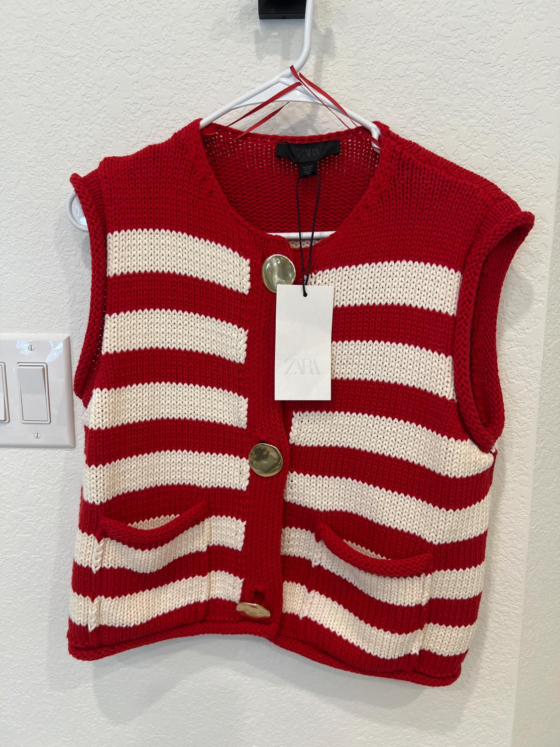 Red knit vest with white stripes and large gold buttons, hanging on a white hanger. Visible tag with "ZARA" text.