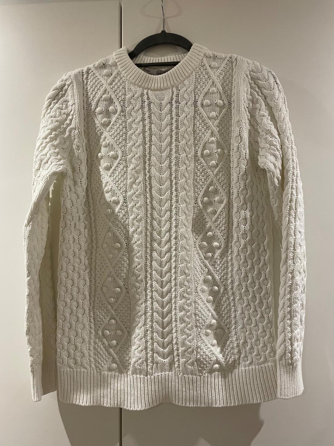 Front view of a white knitted jumper with a cable knit design and a crew neck