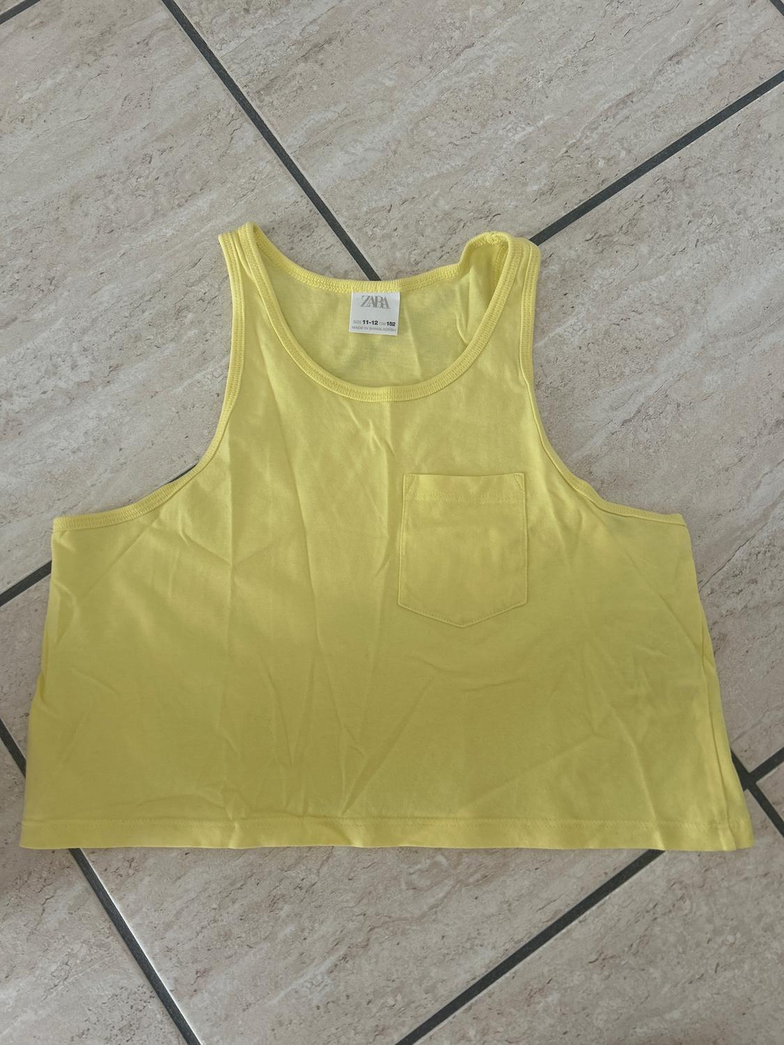 Yellow sleeveless top with front pocket on light tiled floor. Visible label with text "ZARA".