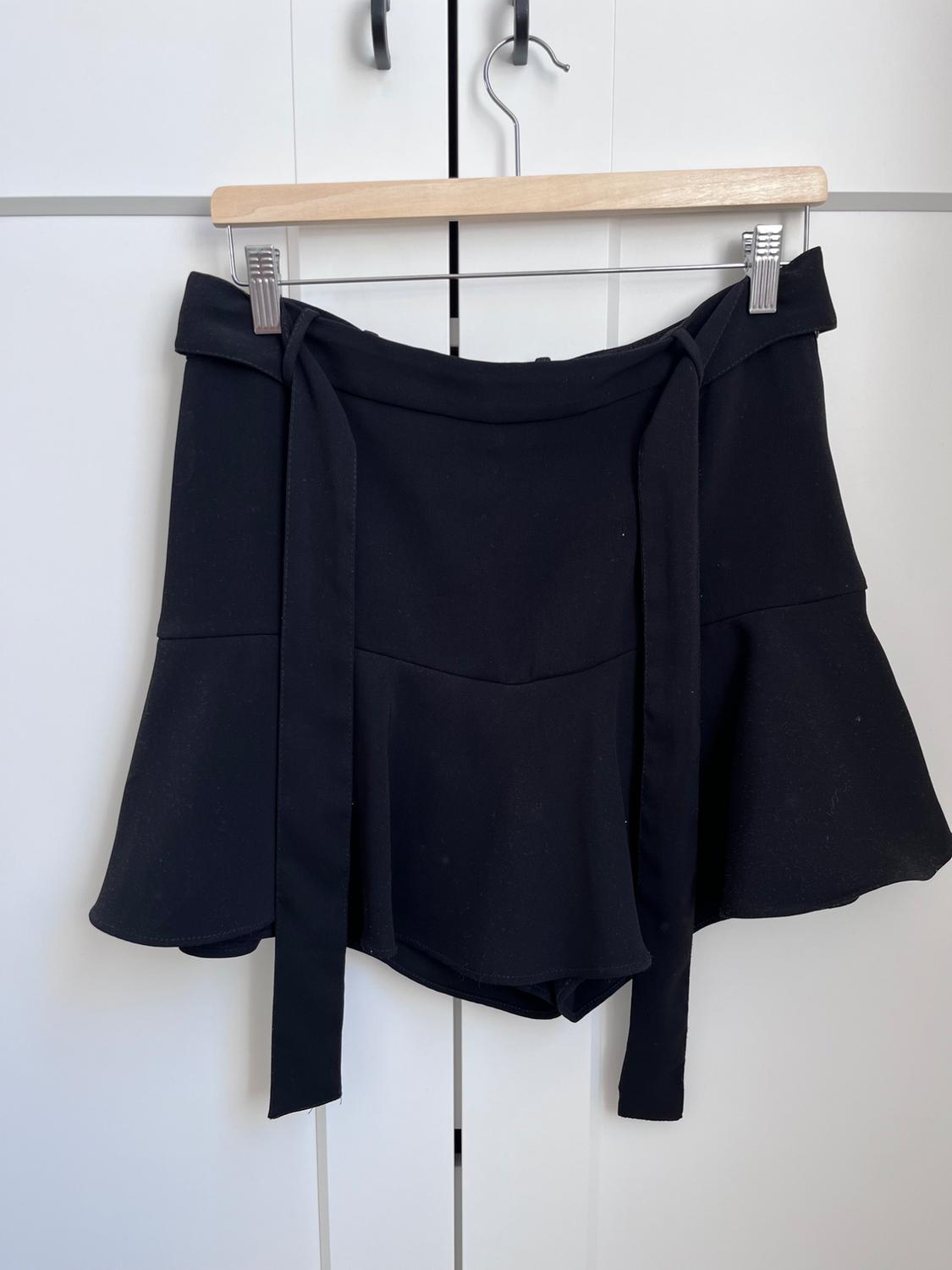 Black tiered ruffle skirt hanging on a wooden hanger in front of a white wardrobe.
