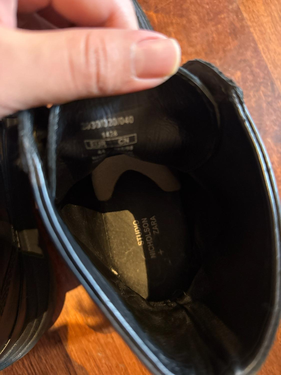 Hand holding the inside of a black shoe. Text: 2033/320/040, 1828, EUR CN and STUDIO NICHOLSON + ZARA on the insole.