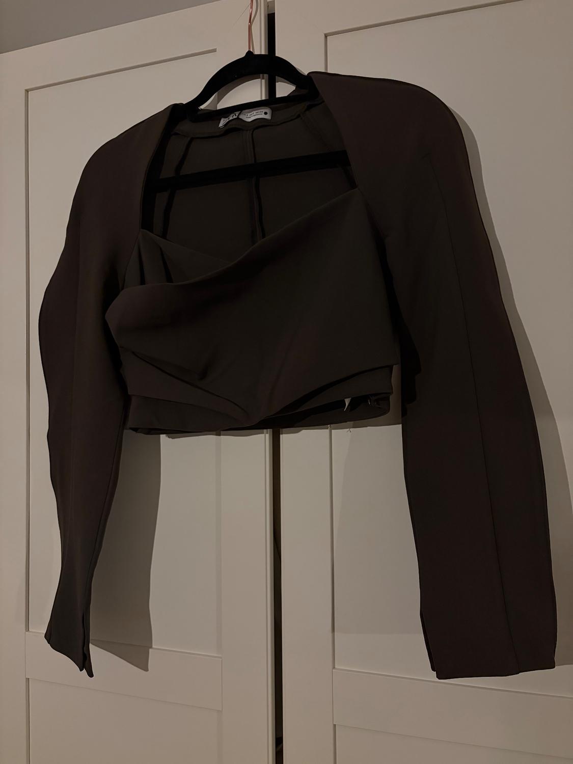 Dark brown jacket hanging on a black hanger in front of a white wardrobe. Dim and minimalist atmosphere.