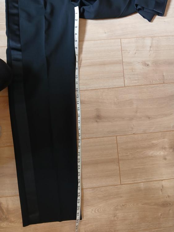 Black trousers on a light wooden floor with a white tape measure alongside, showing measurements in centimetres.