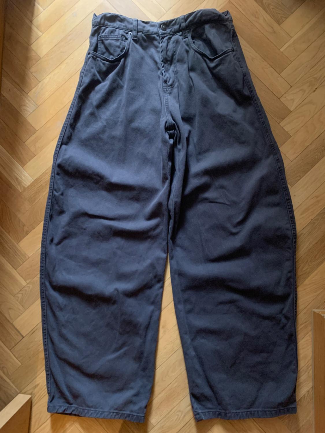 Dark grey extra-wide leg jeans, laid out on a herringbone wooden floor. Casual style.