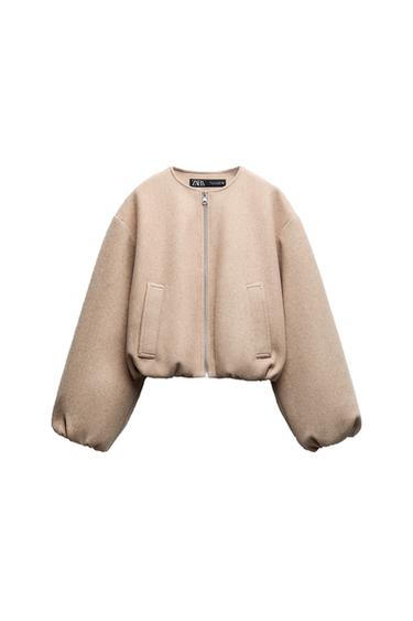 Front view of a beige jacket with a front zipper and side pockets.