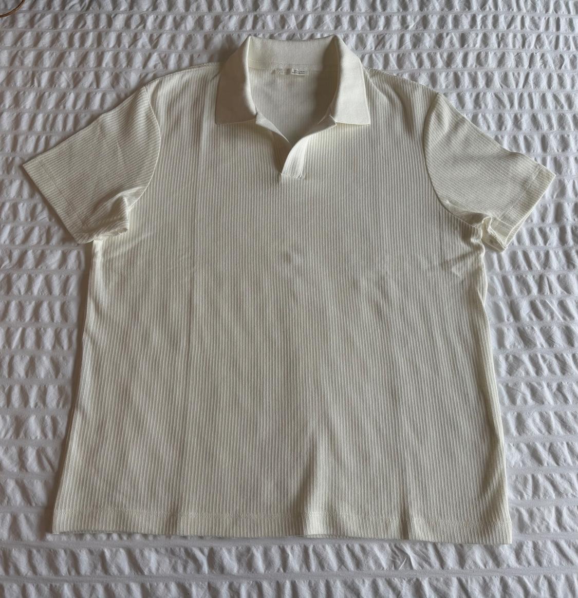 Short-sleeve white polo shirt with a ribbed texture, laid out on a textured white fabric surface.