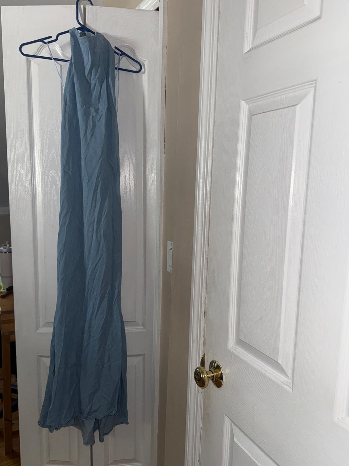 Wrinkled light blue maxi dress hanging on a blue hanger over ajar white door in an interior setting.