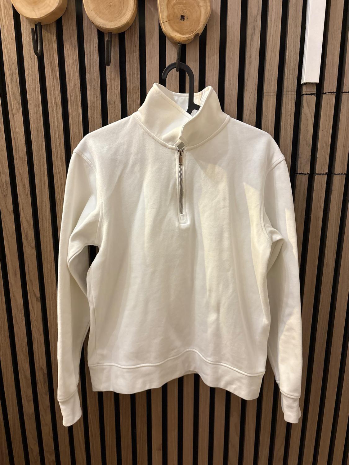 White sweatshirt with a zip neck hanging on a black hook against a vertical wooden slat wall.