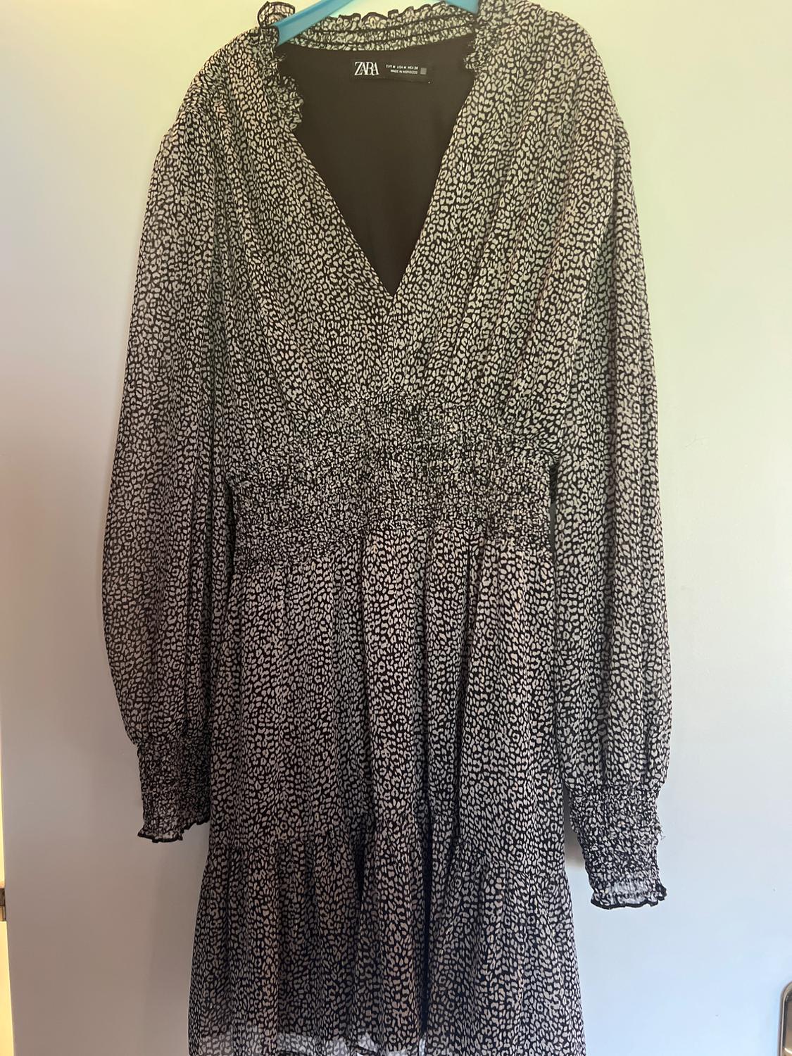 ZARA long-sleeved dress with black and white animal print, V-neck and elasticated waist, hanging on a blue hanger against a white background.