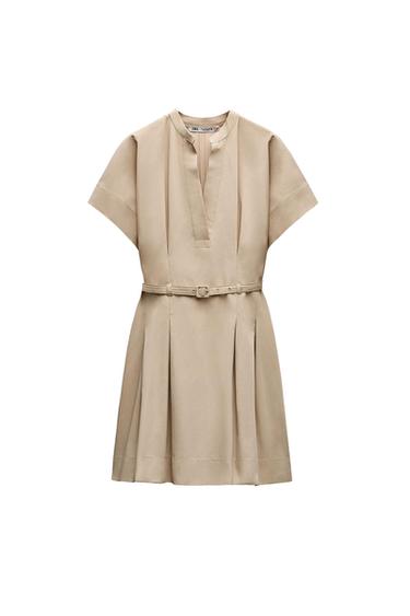 Short beige dress with short sleeves, V-neck, matching belt and pleated skirt against a white background. ZARA label.