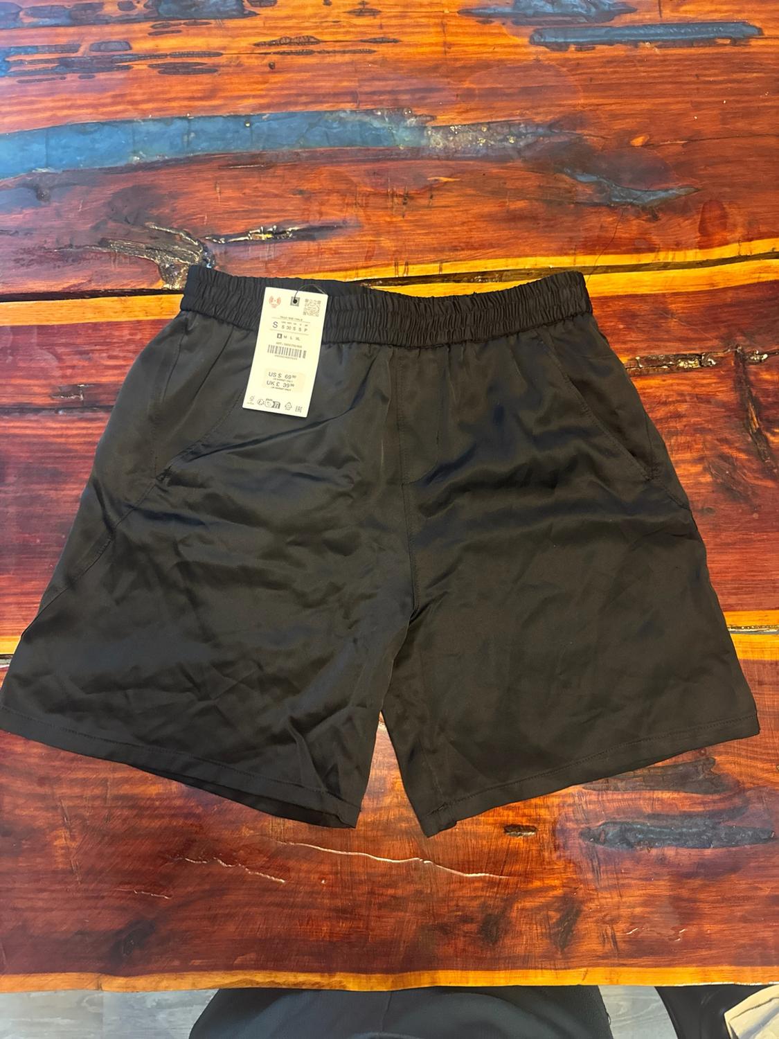 Black sports shorts with an elasticated waistband and label, presented on a rustic wooden table with a visible grain.