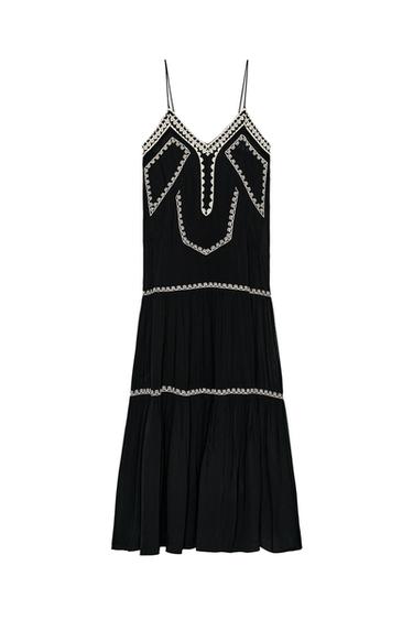 Front view of a long black dress with white embroidery on a V-neckline and thin straps. Flared hem.