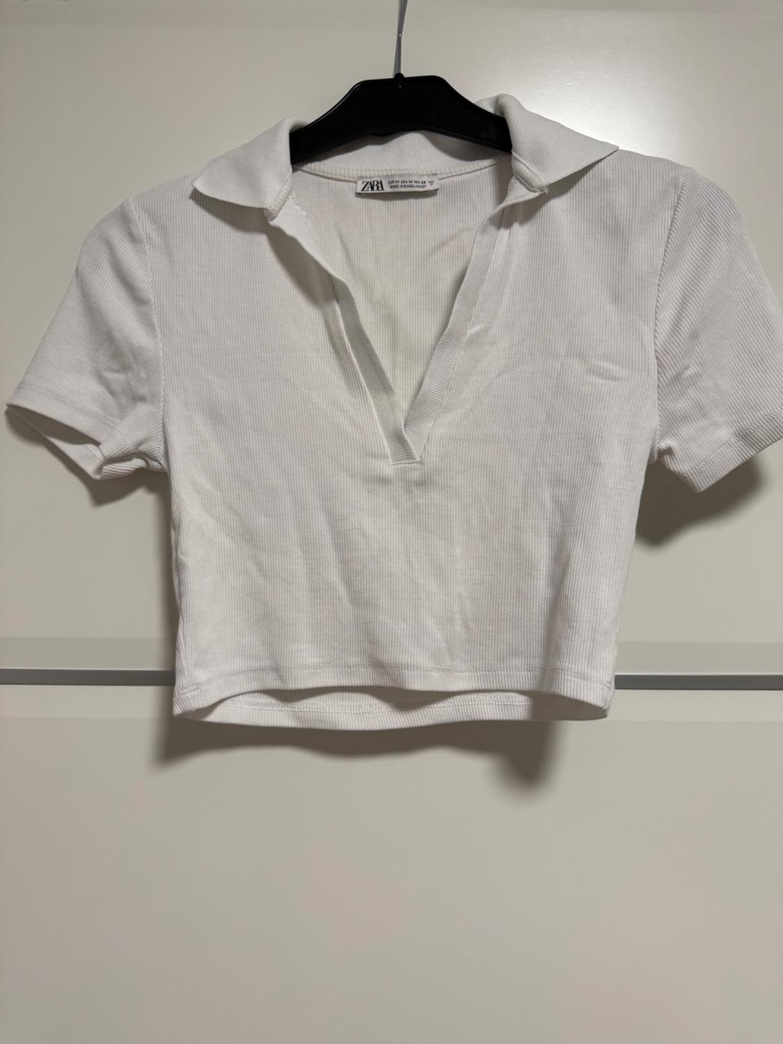 White short-sleeved polo shirt, hanging on a black hanger against a white background. Label visible on the collar.