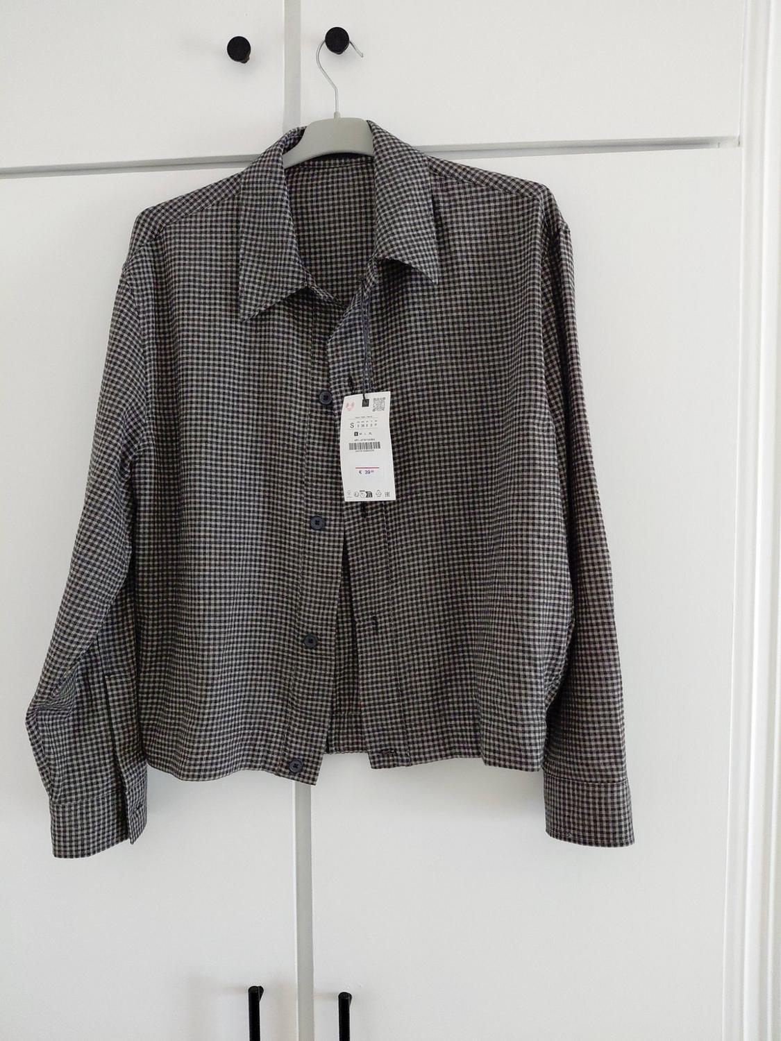Long-sleeved checked shirt, buttoned up and with a label, hanging on a hanger above a white wardrobe.