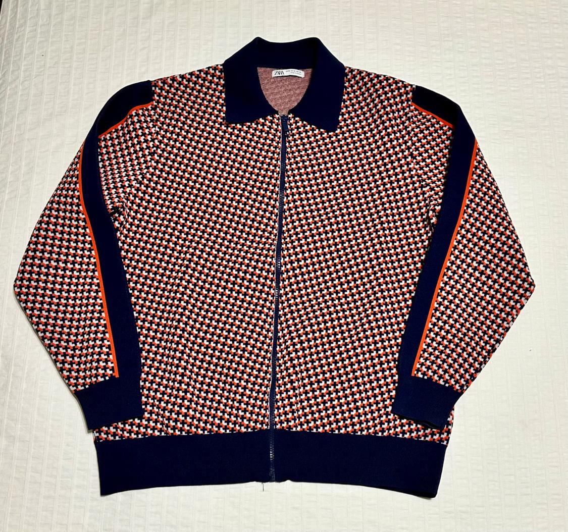 Geometric print jacket in red, white, and black, with a front zip and a dark blue collar on a white background.
